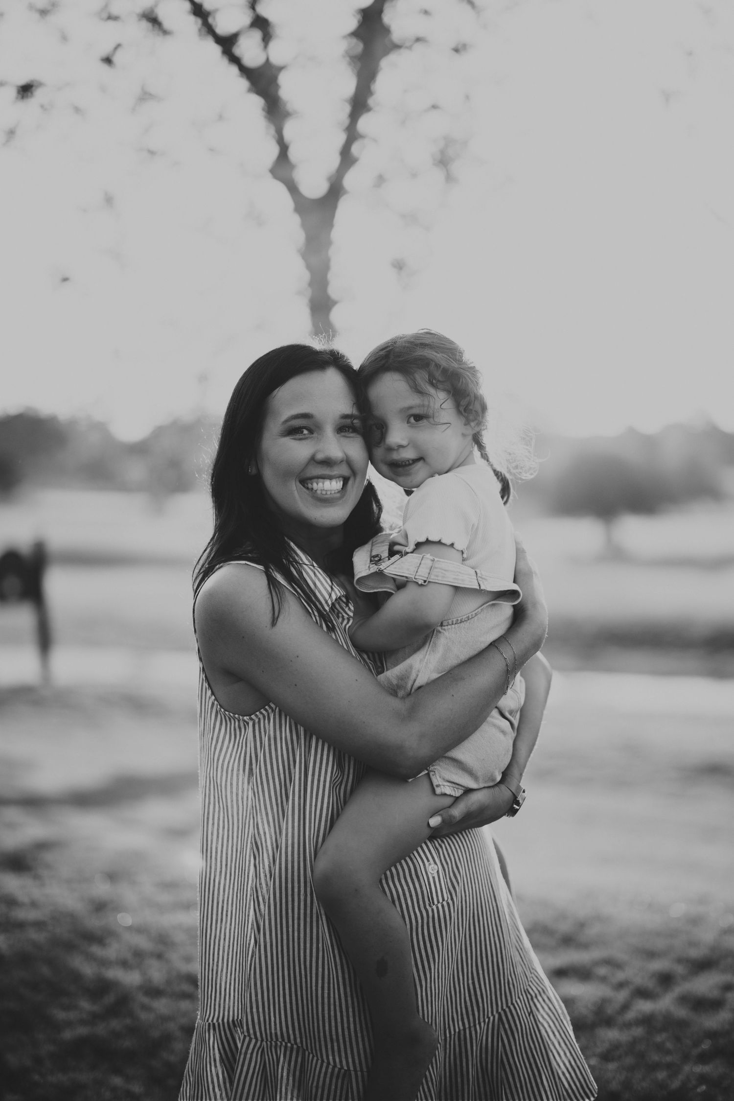 Black and white photo of a smiling woman in a striped dress holding a young child outdoors.