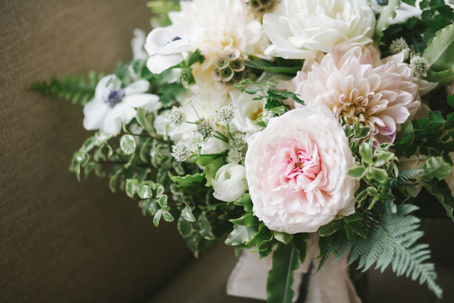 Elegant bridal bouquet with blush pink roses, white anemones, dahlias, and lush greenery.