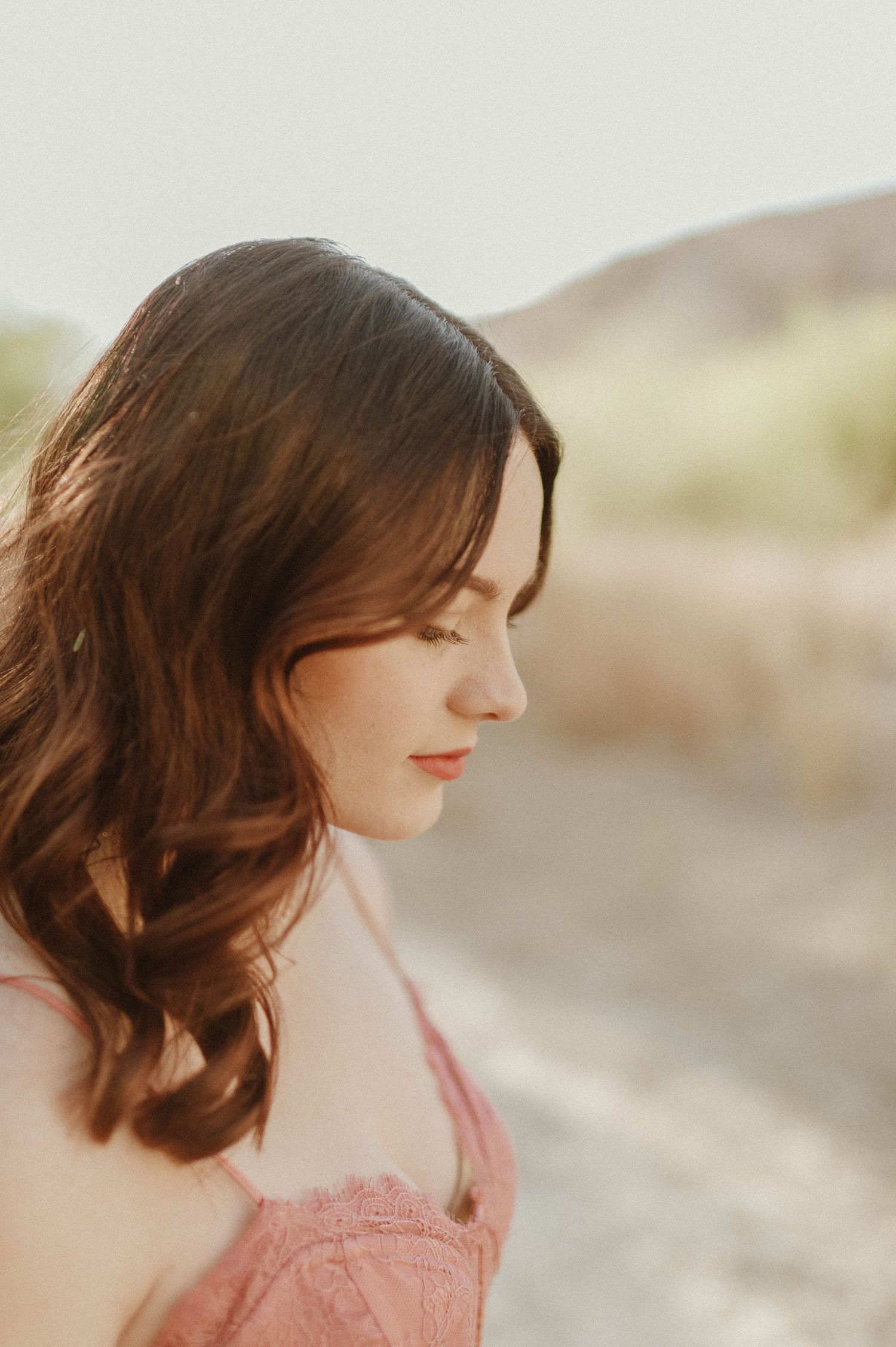Side profile of brunette woman in pink dress with soft glowing backlit outdoor background.