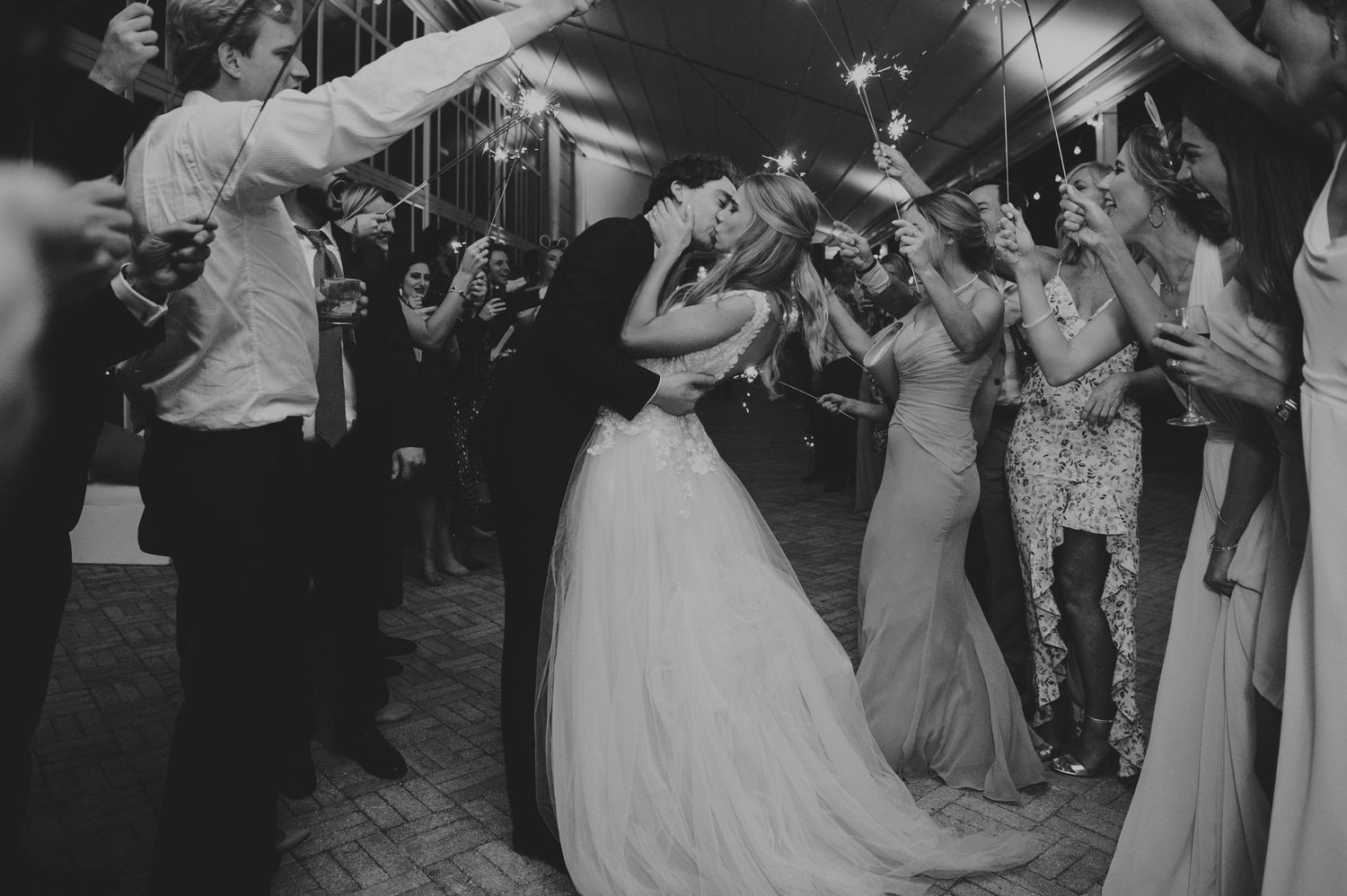 Black and white wedding sparkler exit with bride and groom kissing surrounded by cheering guests.
