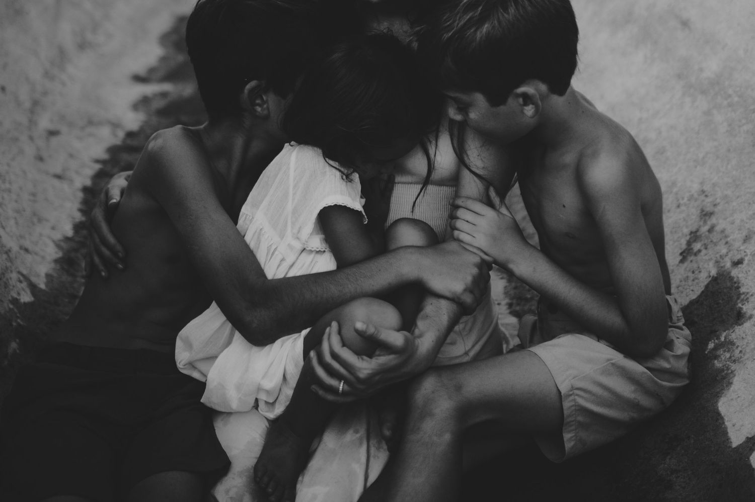 Black and white image of three children huddled together looking down at something.