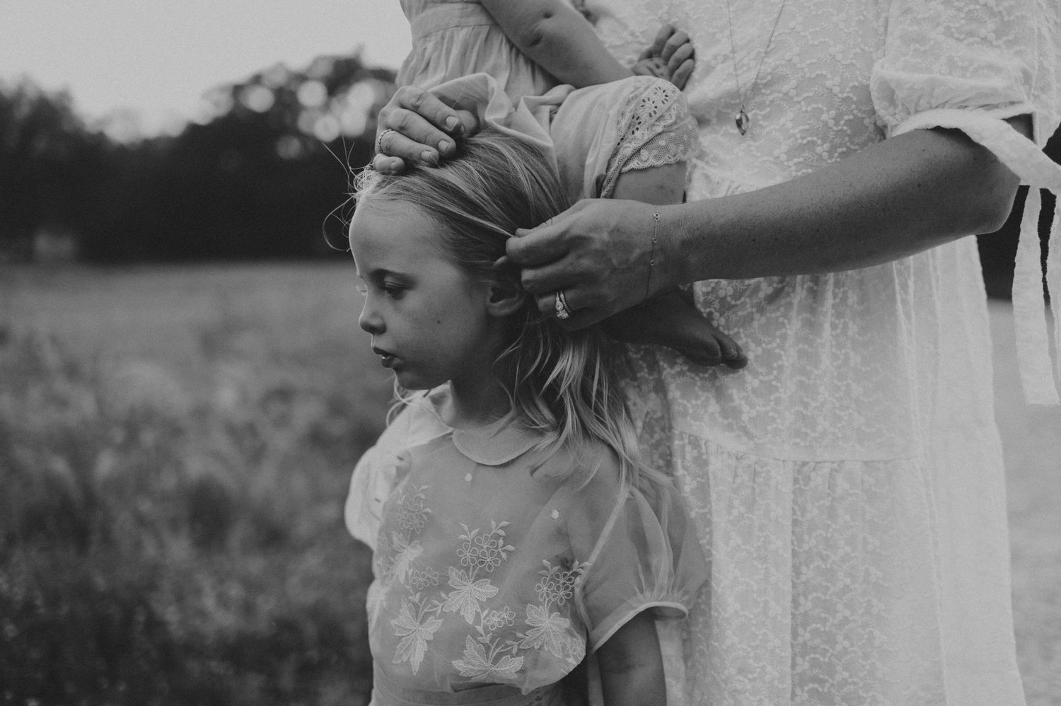 Black and white photo of a woman braiding a young girl's hair outdoors in a field.