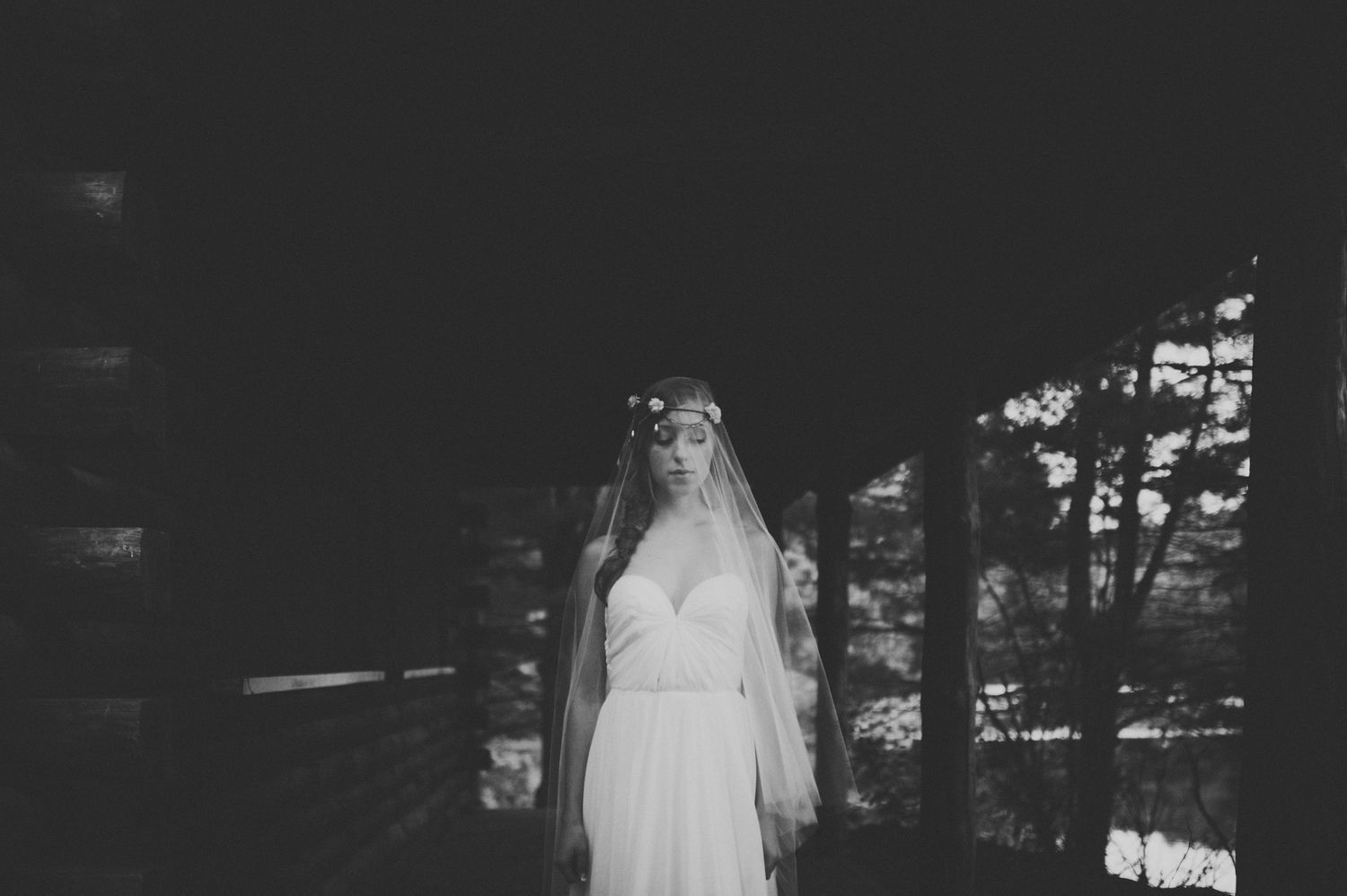 Black and white portrait of bride in white dress and veil standing in dark rustic setting.