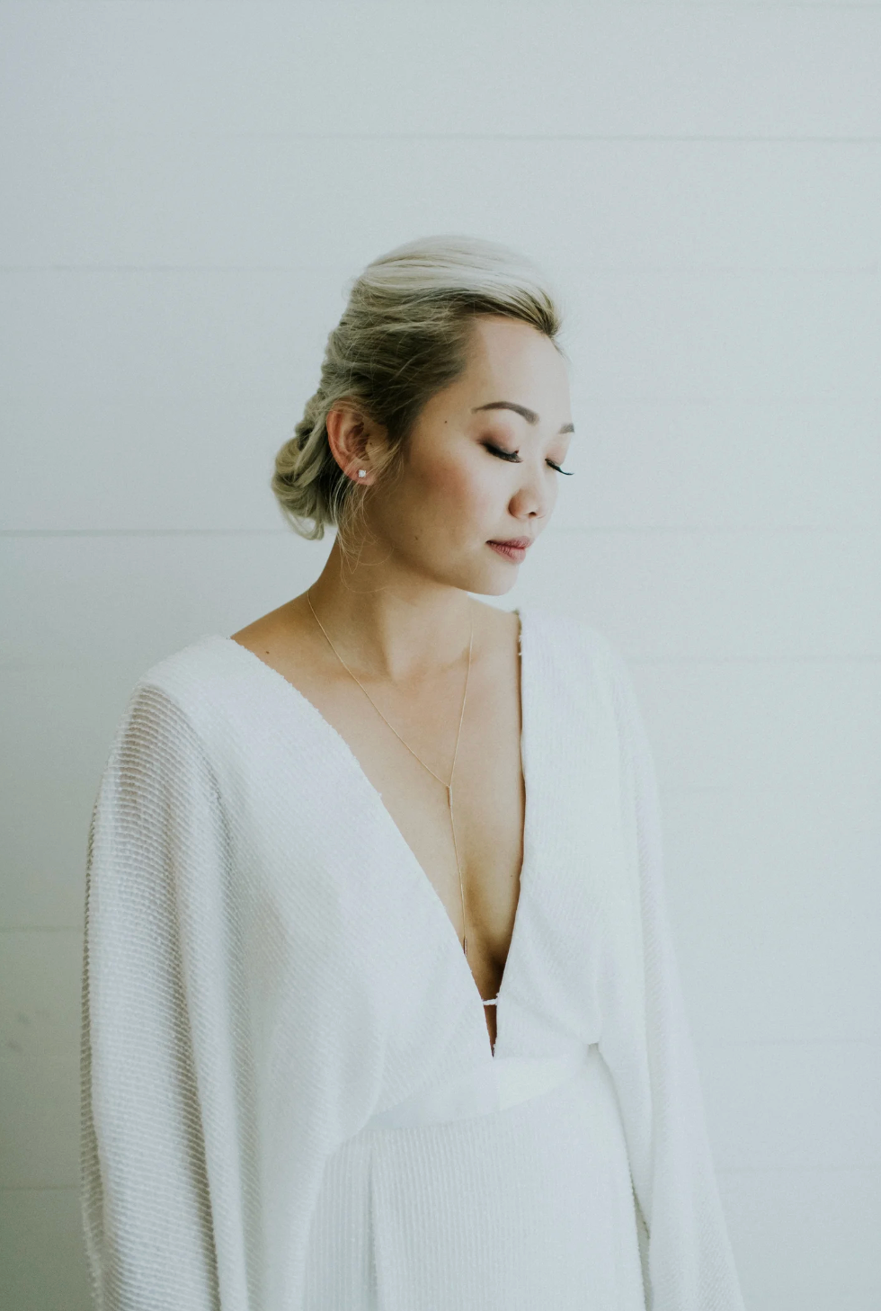Elegant bride in a deep V-neck white wedding dress with updo hairstyle and pearl earrings.