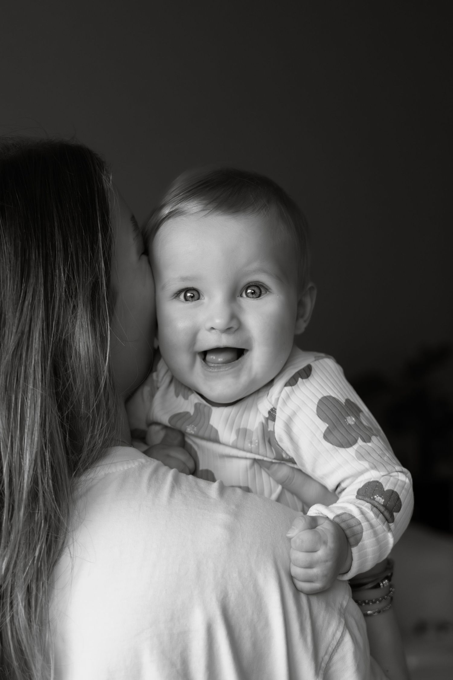 Zwart-wit portret van lachende baby op de arm van moeder, newborn fotografie door Eva Berendse