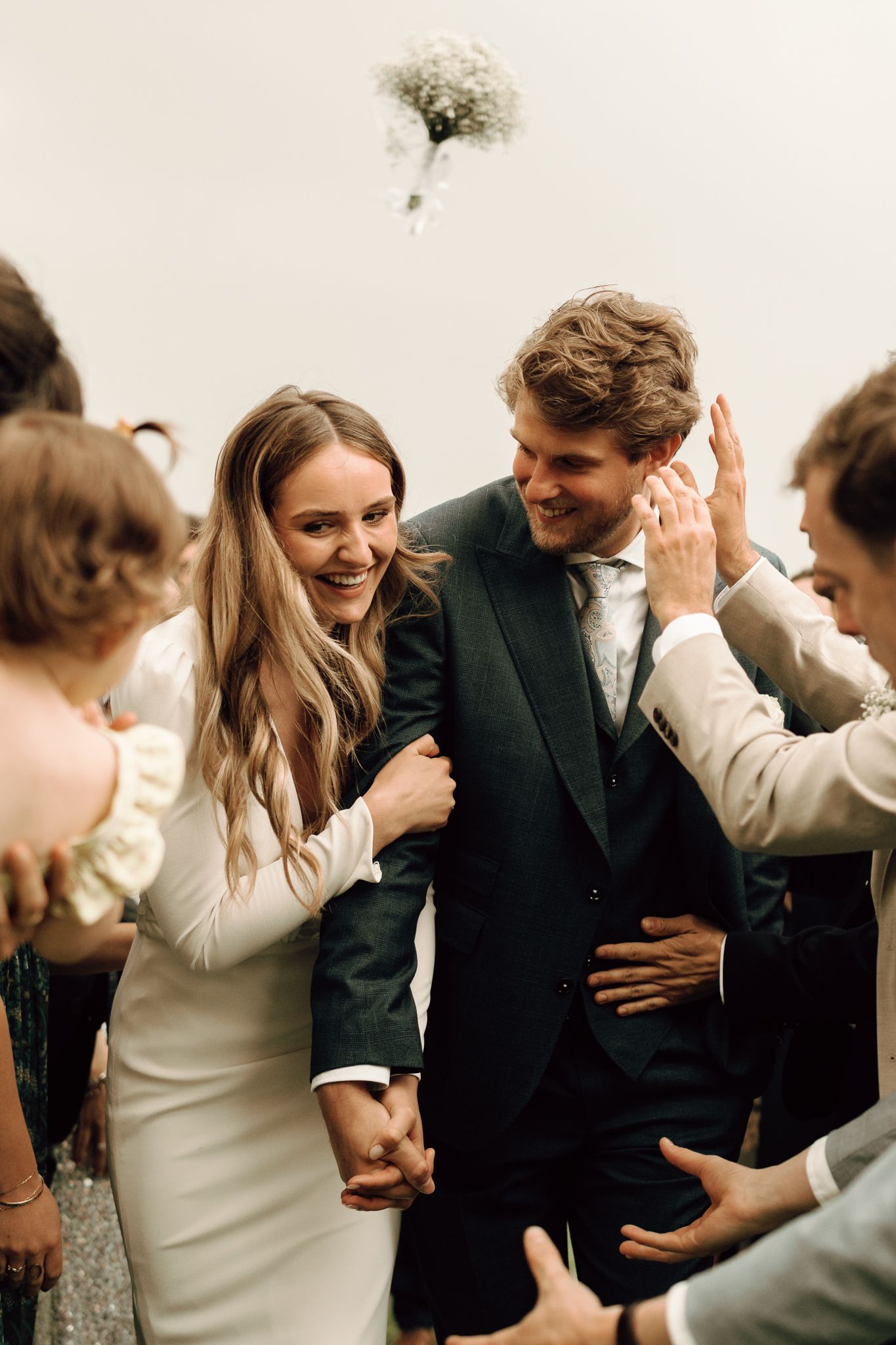 Joyful bride and groom walk through guests after wedding ceremony while bouquet is tossed in the air.