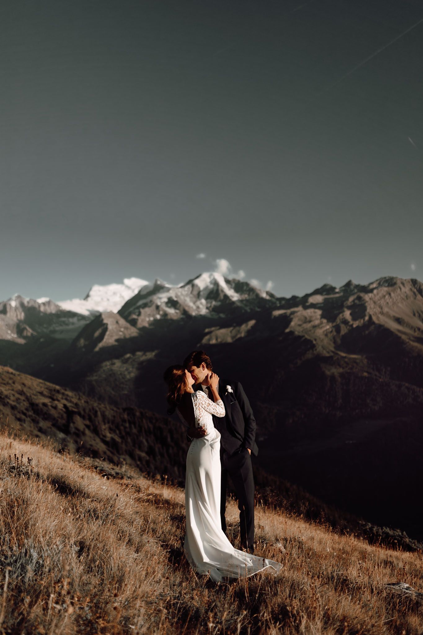 Bride and groom kissing on a mountain peak with snow-capped Alps in the background during their wedding elopement.