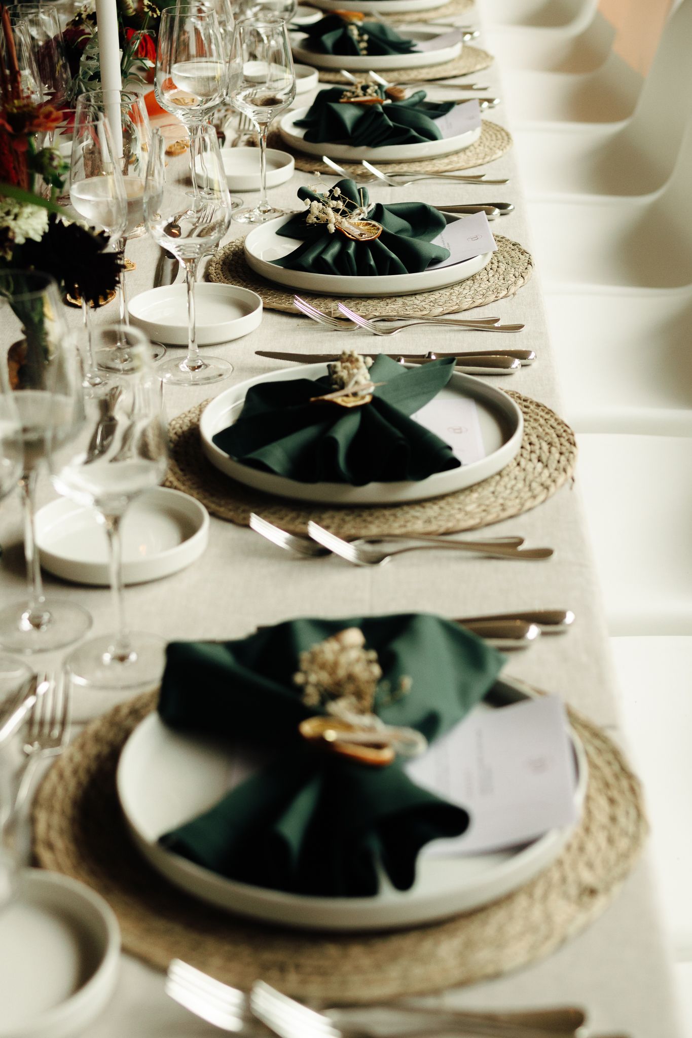 Elegant wedding reception table set with green napkins, woven placemats, and crystal glasses.