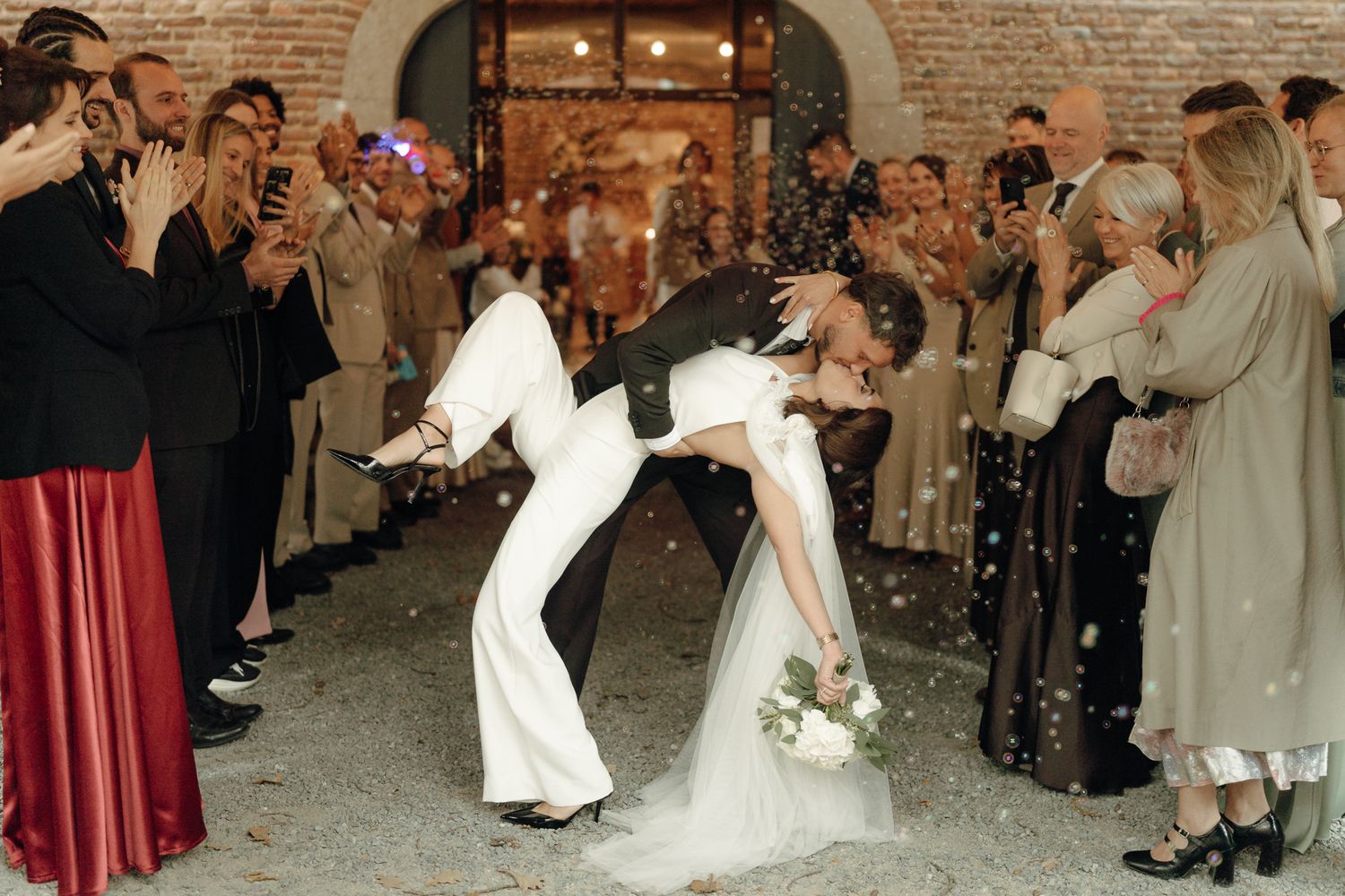Bride and groom share a romantic dip kiss while guests toss confetti at an elegant wedding venue.