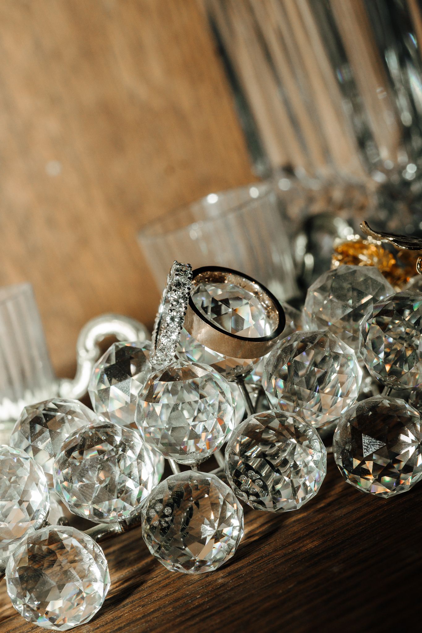 Crystal decorative spheres and diamond rings arranged on a wooden surface with glassware in the background.