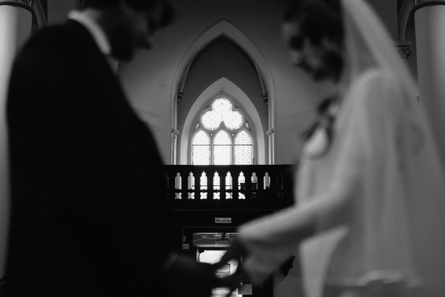 Black and white photo of bride and groom at church altar with Gothic stained glass window.