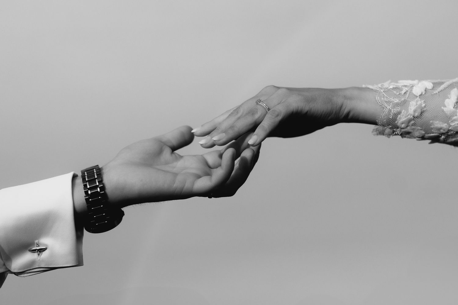 Black and white photo of bride and groom reaching out to hold hands tenderly.