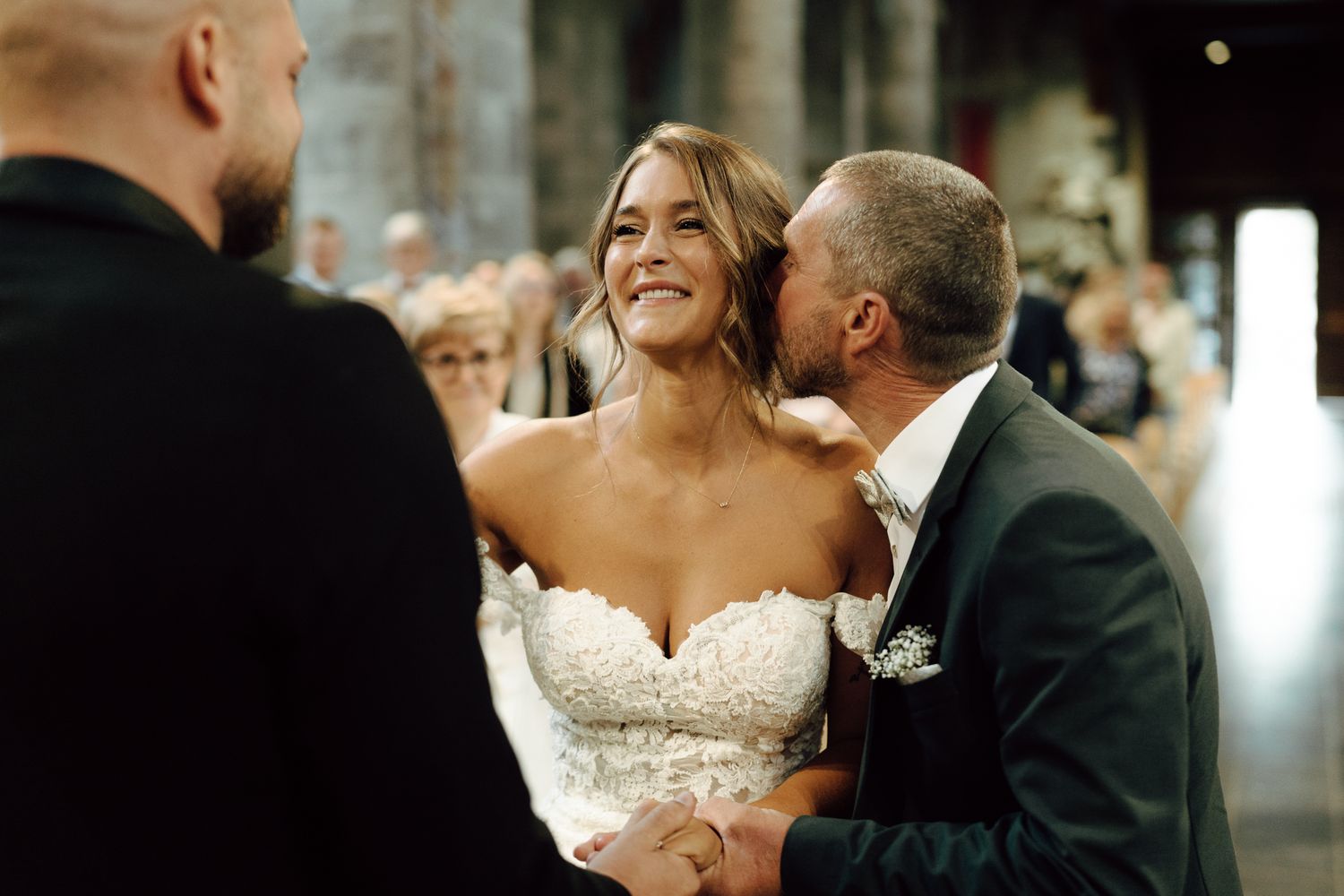 Father of bride kisses her cheek as groom stands at church altar.