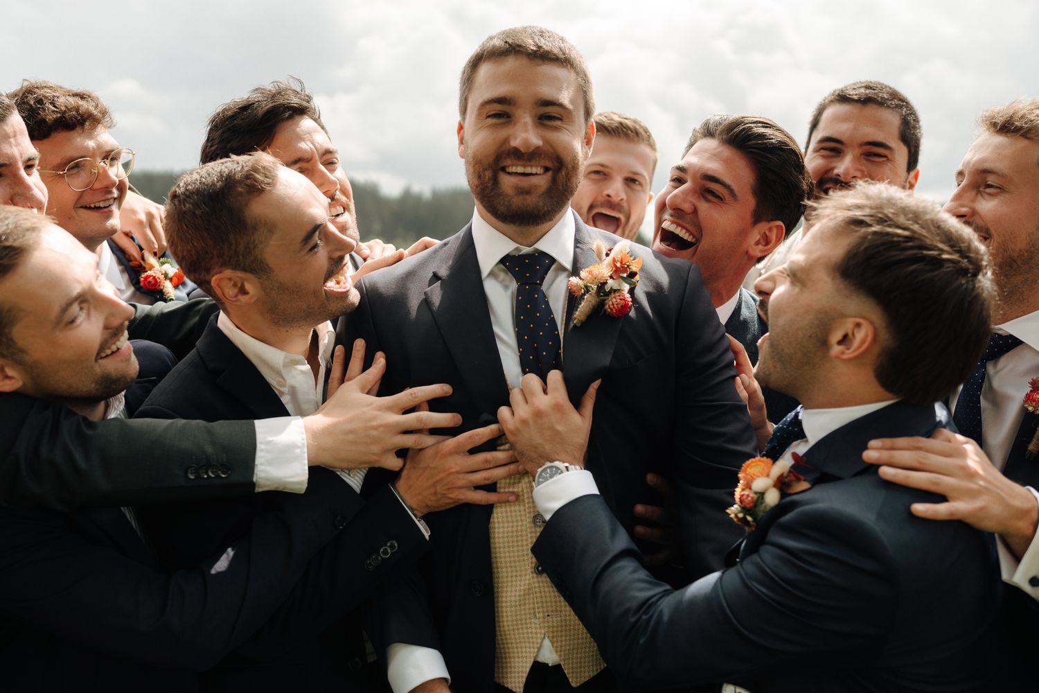 Smiling groom surrounded by cheerful groomsmen in navy suits celebrating at wedding.