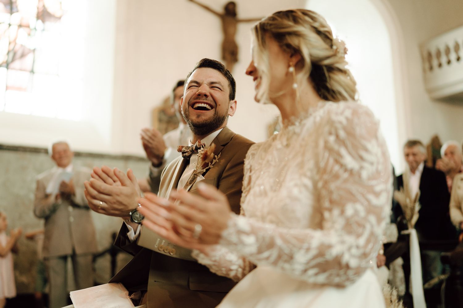 Joyful bride and groom laughing and clapping together during wedding ceremony in church.