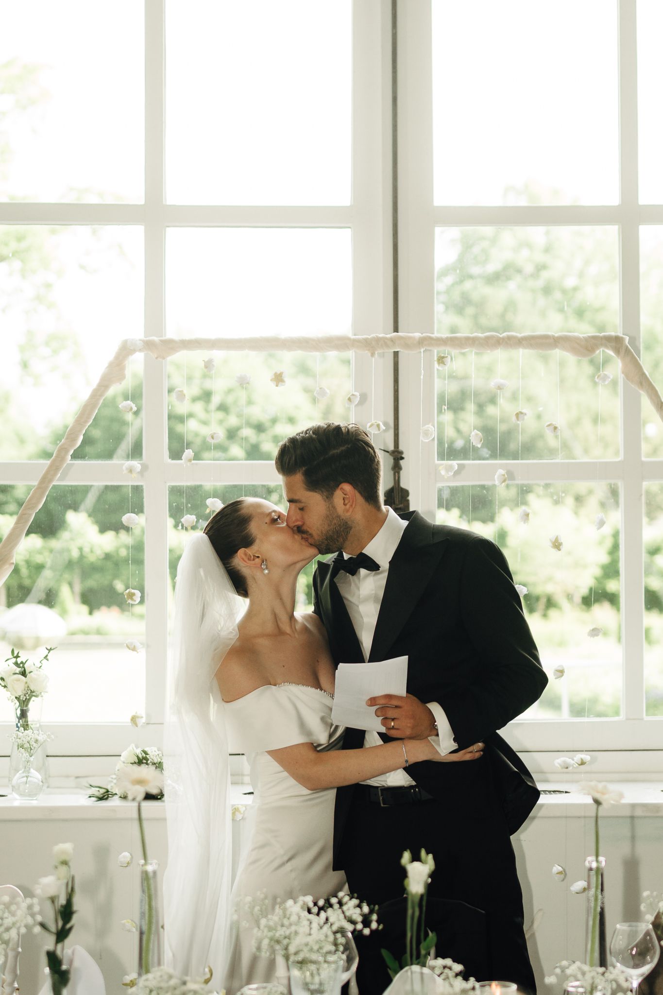 Bride and groom kissing at altar in bright sunlit wedding venue.