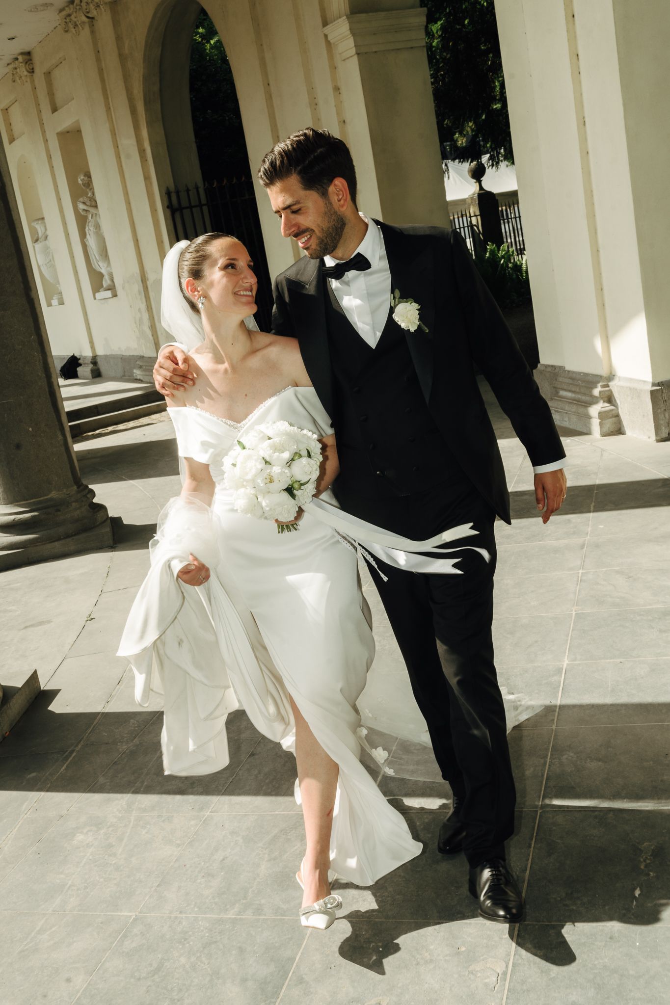 Smiling bride and groom walking together outside elegant white building.