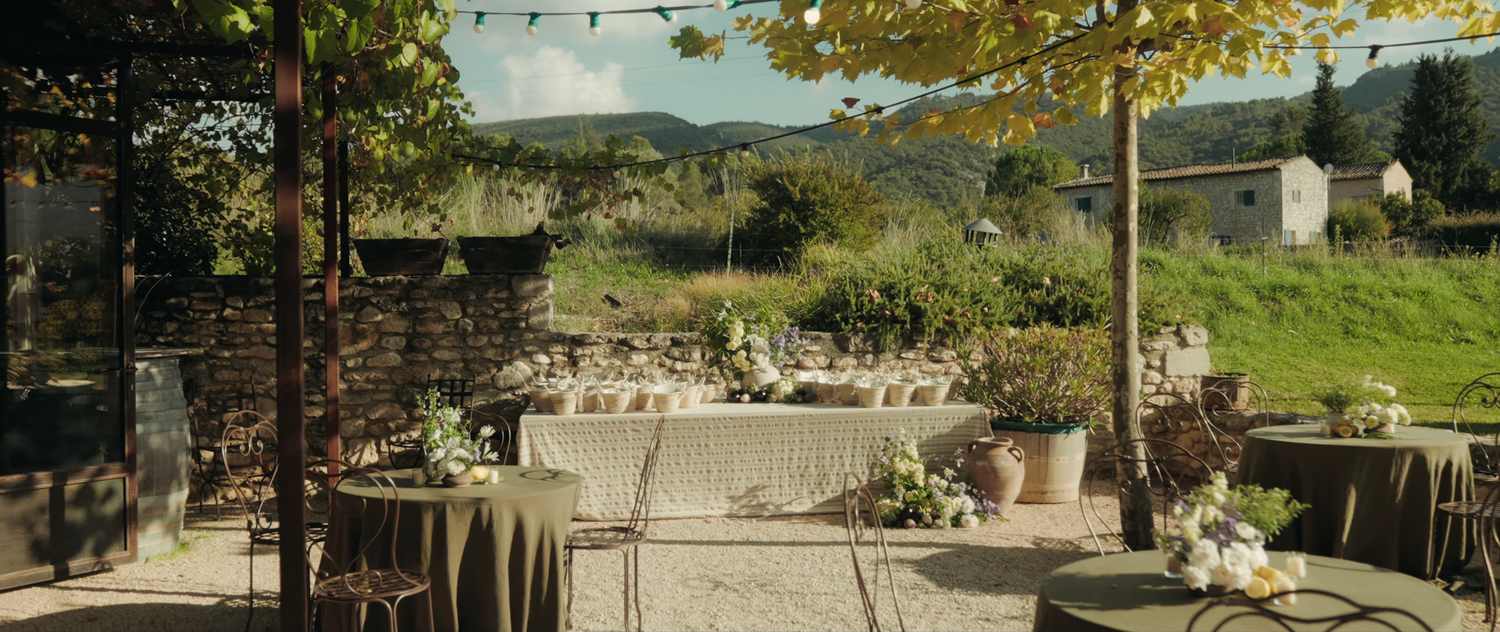 Elegant outdoor wedding reception setup with rustic stone walls, draped tables, and lush greenery under string lights.