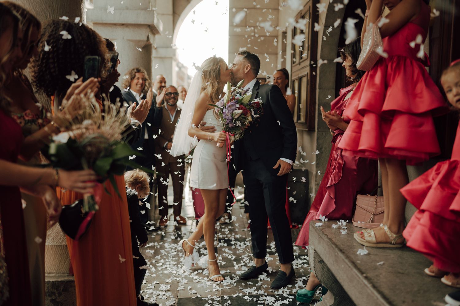 Newlyweds kissing as confetti showers them while exiting wedding ceremony venue.