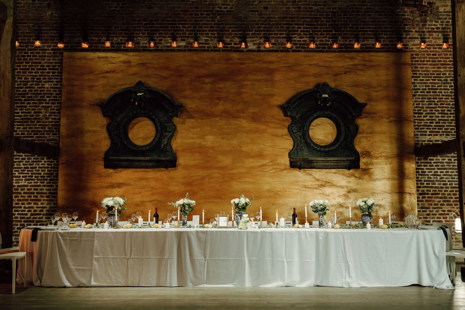 Rustic wedding reception hall with long white head table, candles, and decorative black wall mirrors.