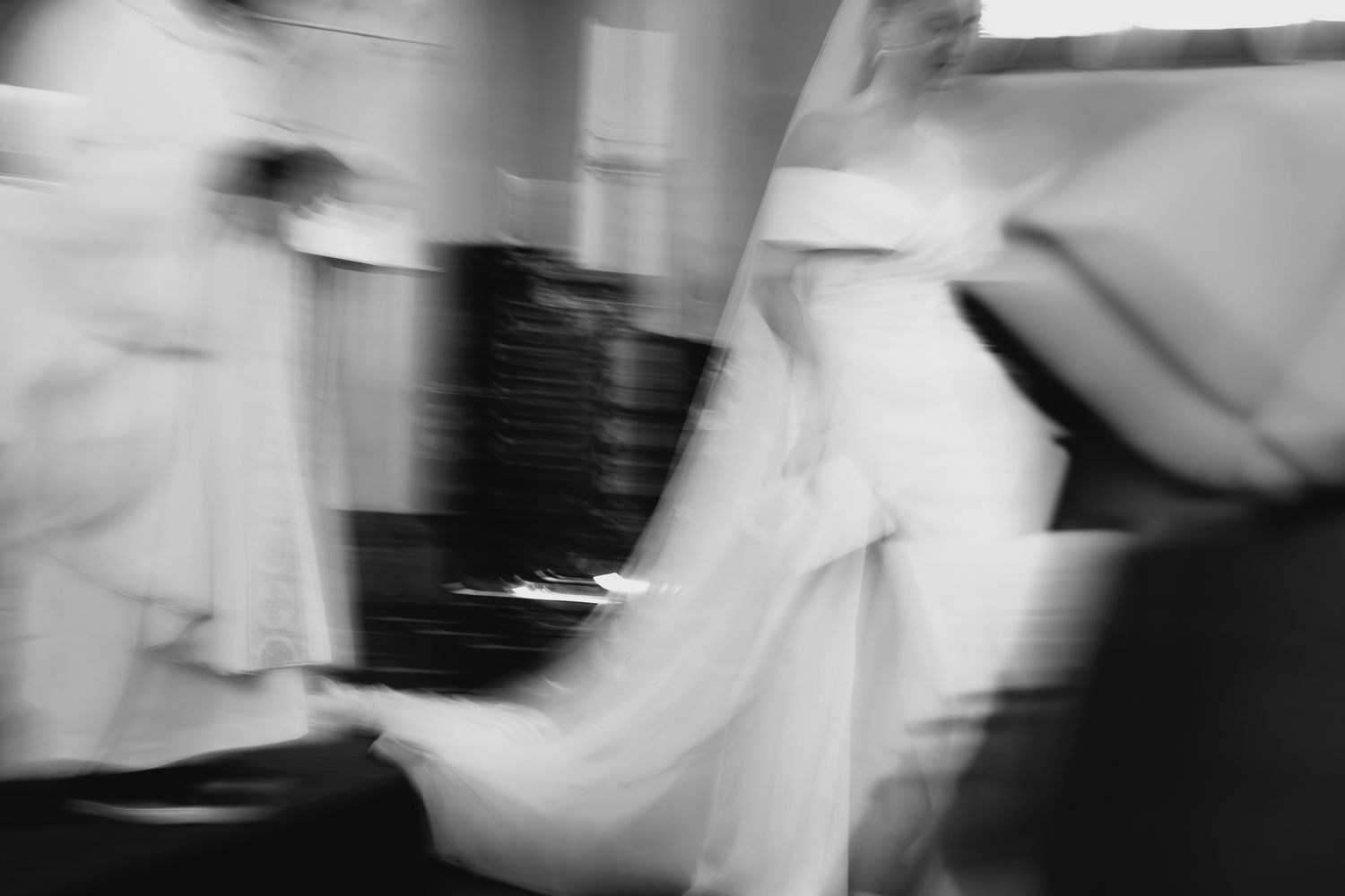 Black and white blurred artistic photo capturing movement of bridal party during wedding ceremony.