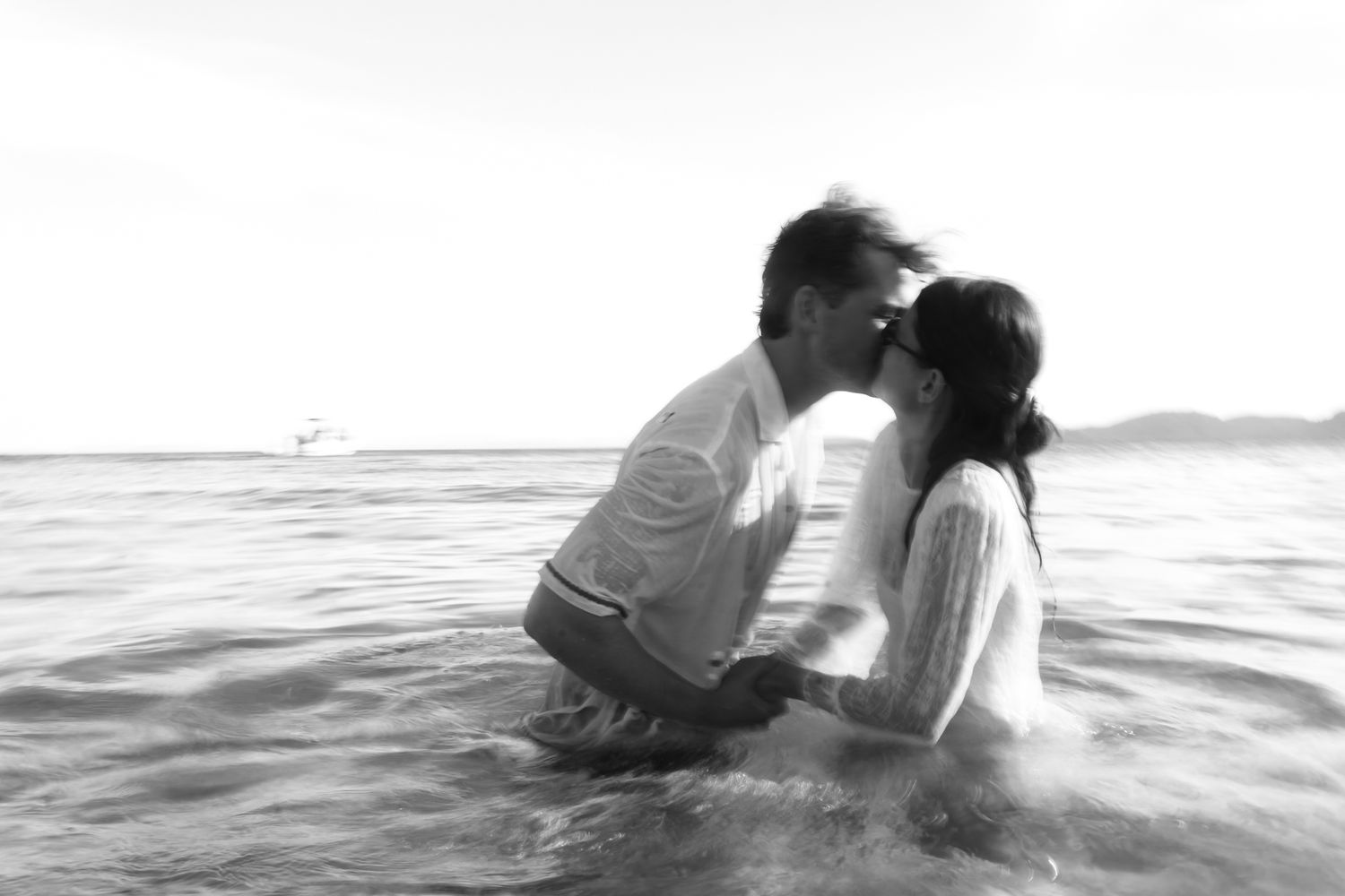 Romantic couple kissing in ocean waves, black and white beach photography.