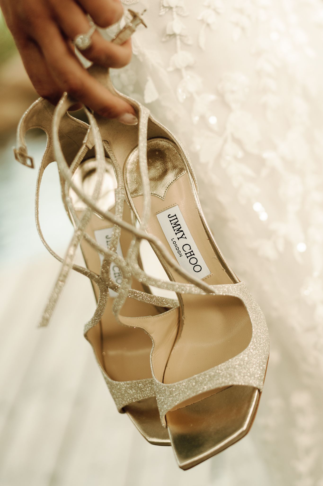 Close-up of glittery Jimmy Choo bridal heels held against white lace wedding dress.