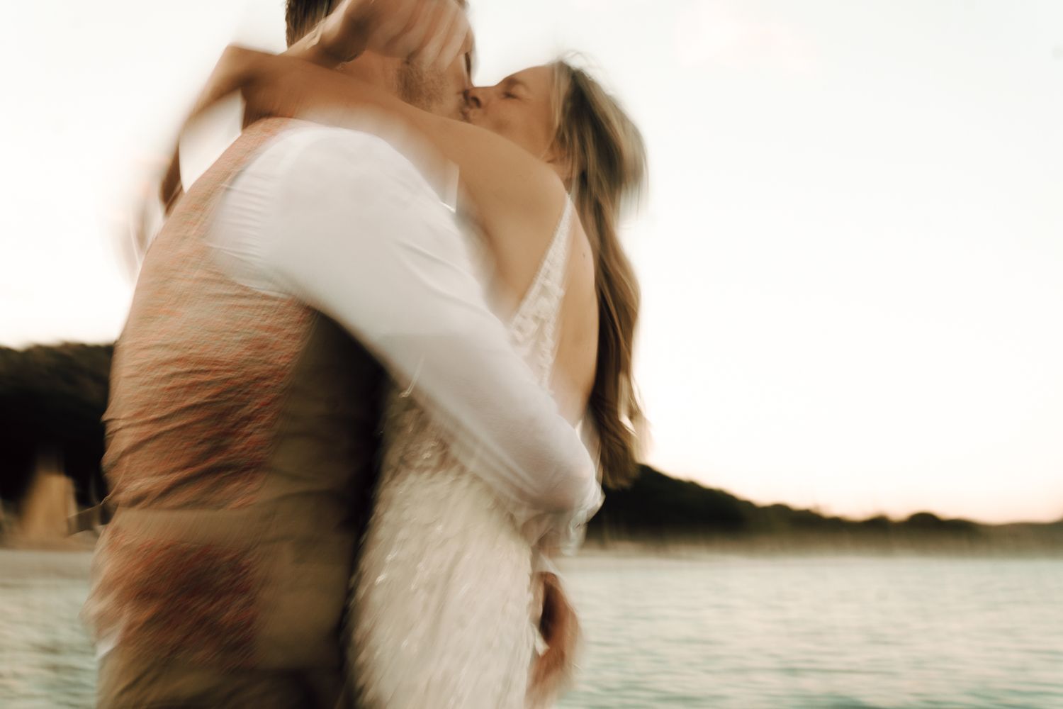 Romantic blurred image of bride and groom sharing kiss by the sea.