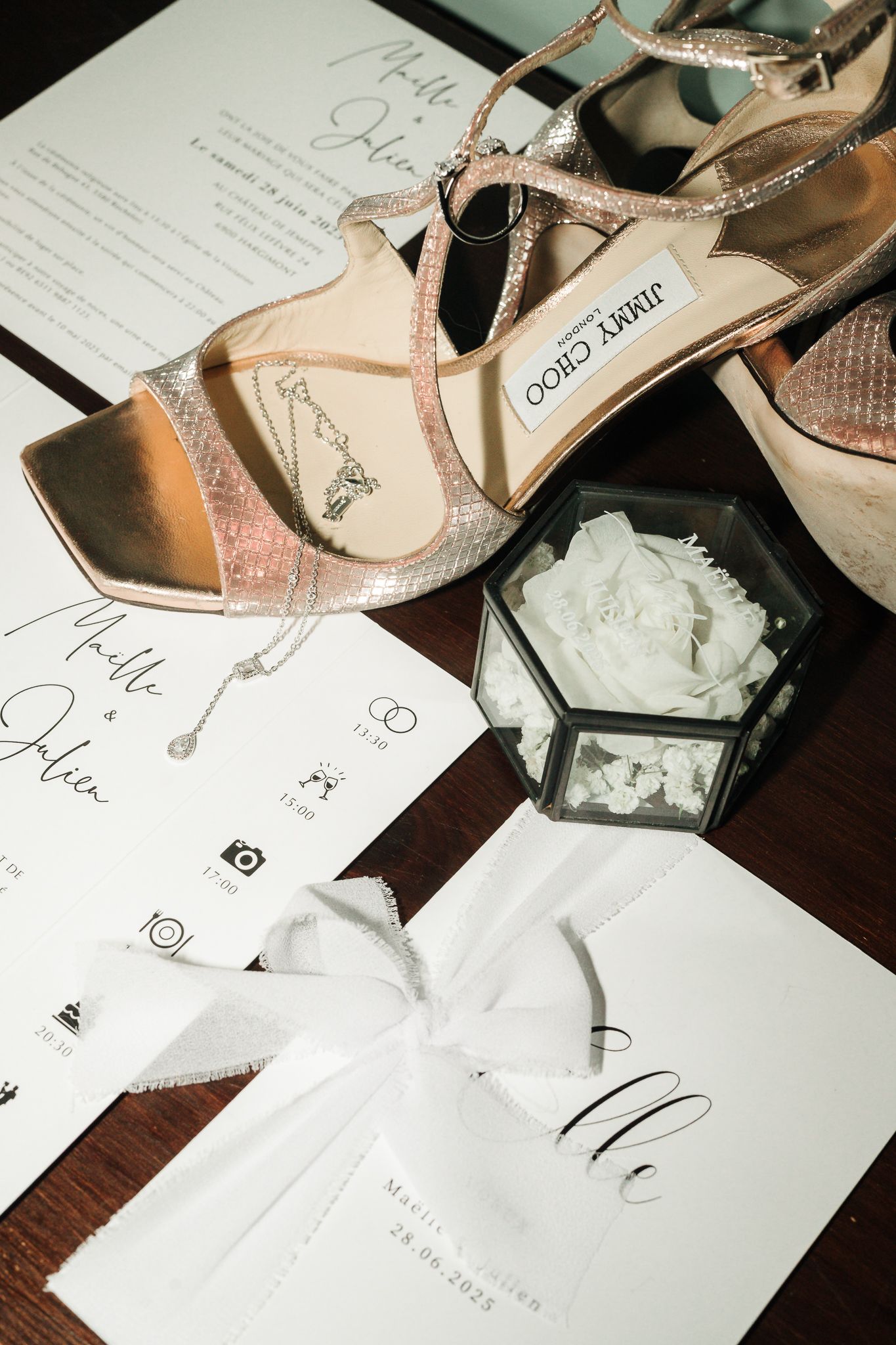 Jimmy Choo bridal heels displayed with wedding stationery, jewelry, and a glass box with white flowers.