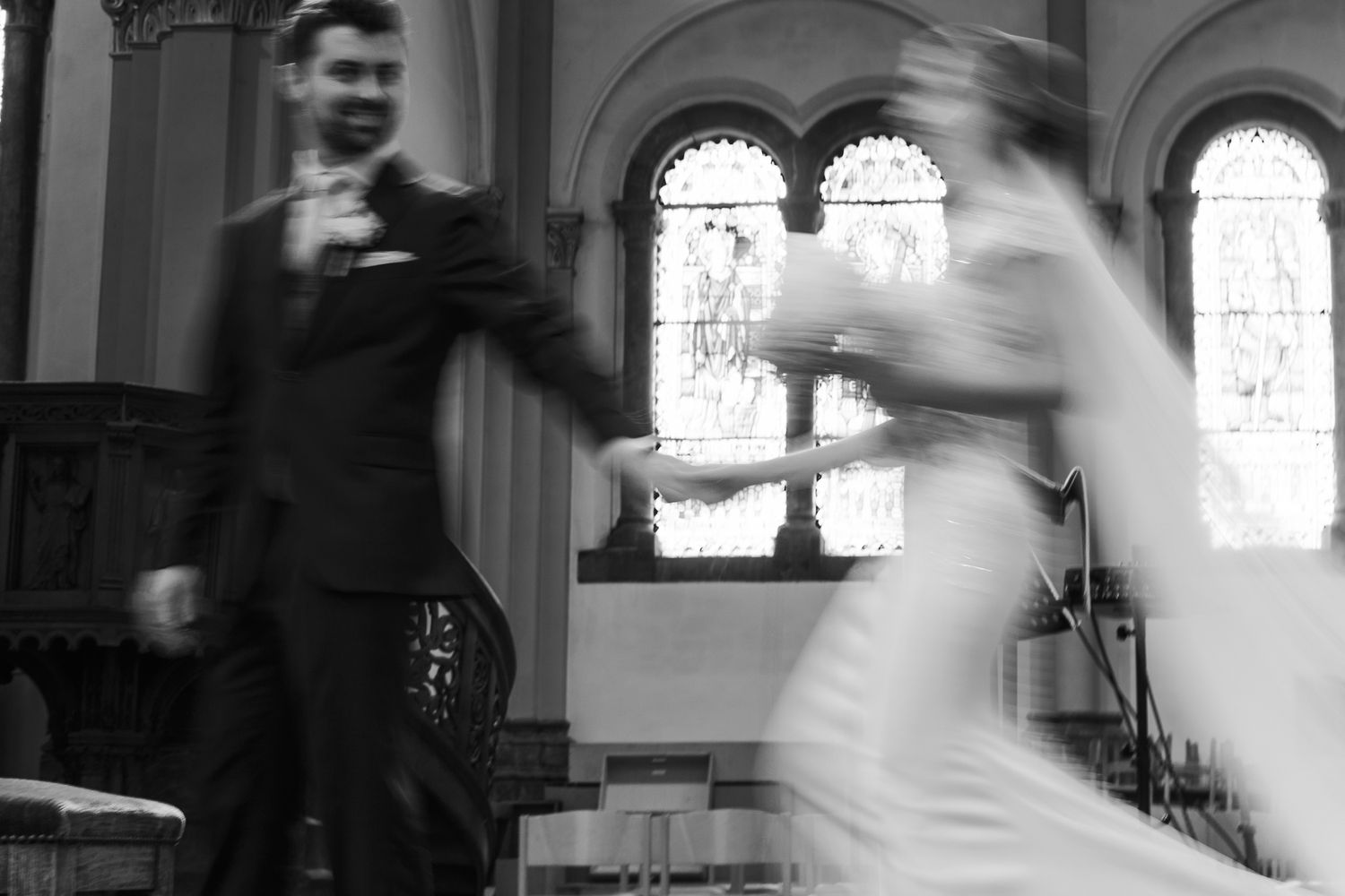 Black and white blurred motion photo of bride and groom dancing in a church during wedding ceremony.