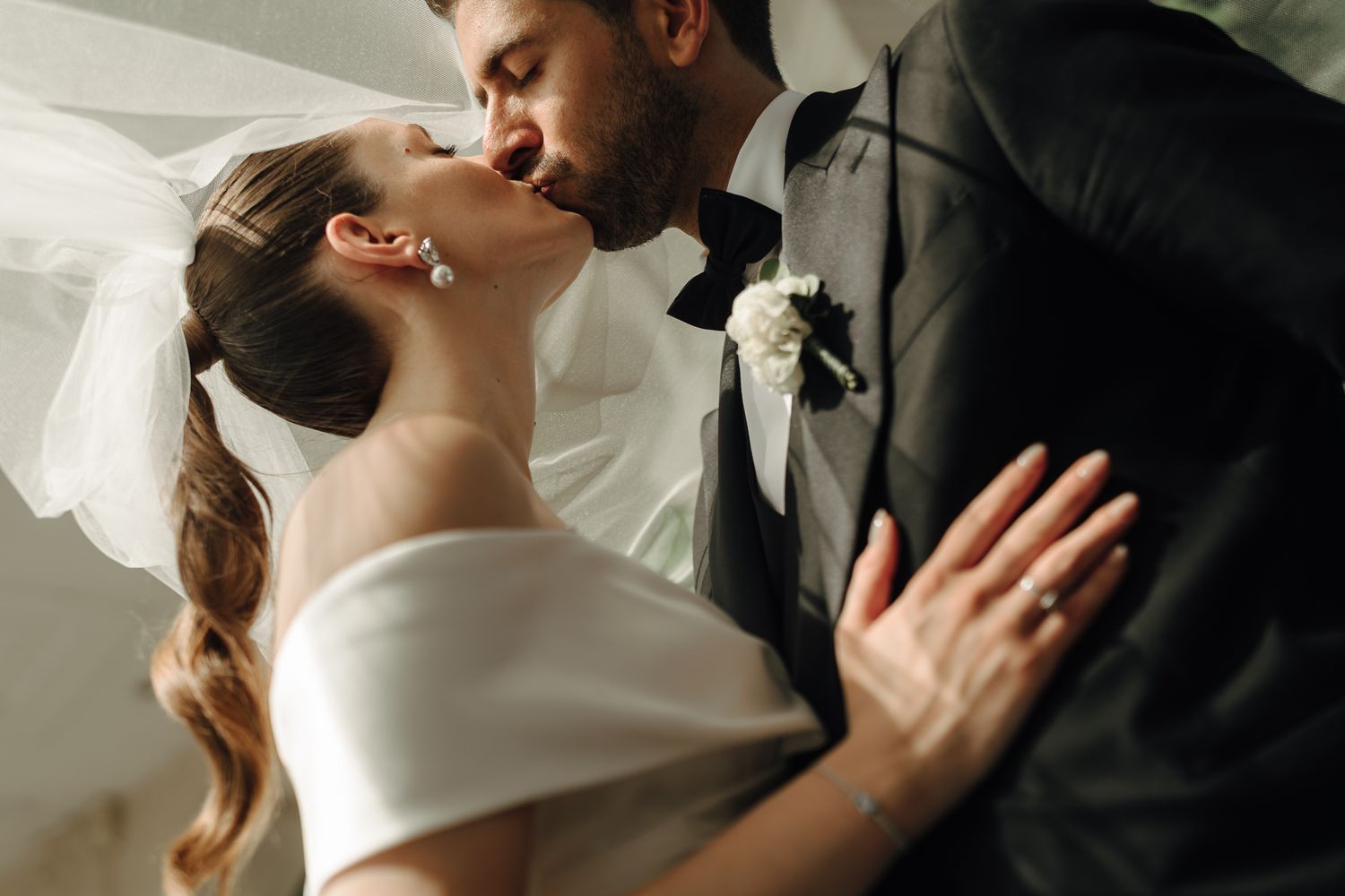 Bride and groom sharing a romantic kiss on their wedding day indoors.