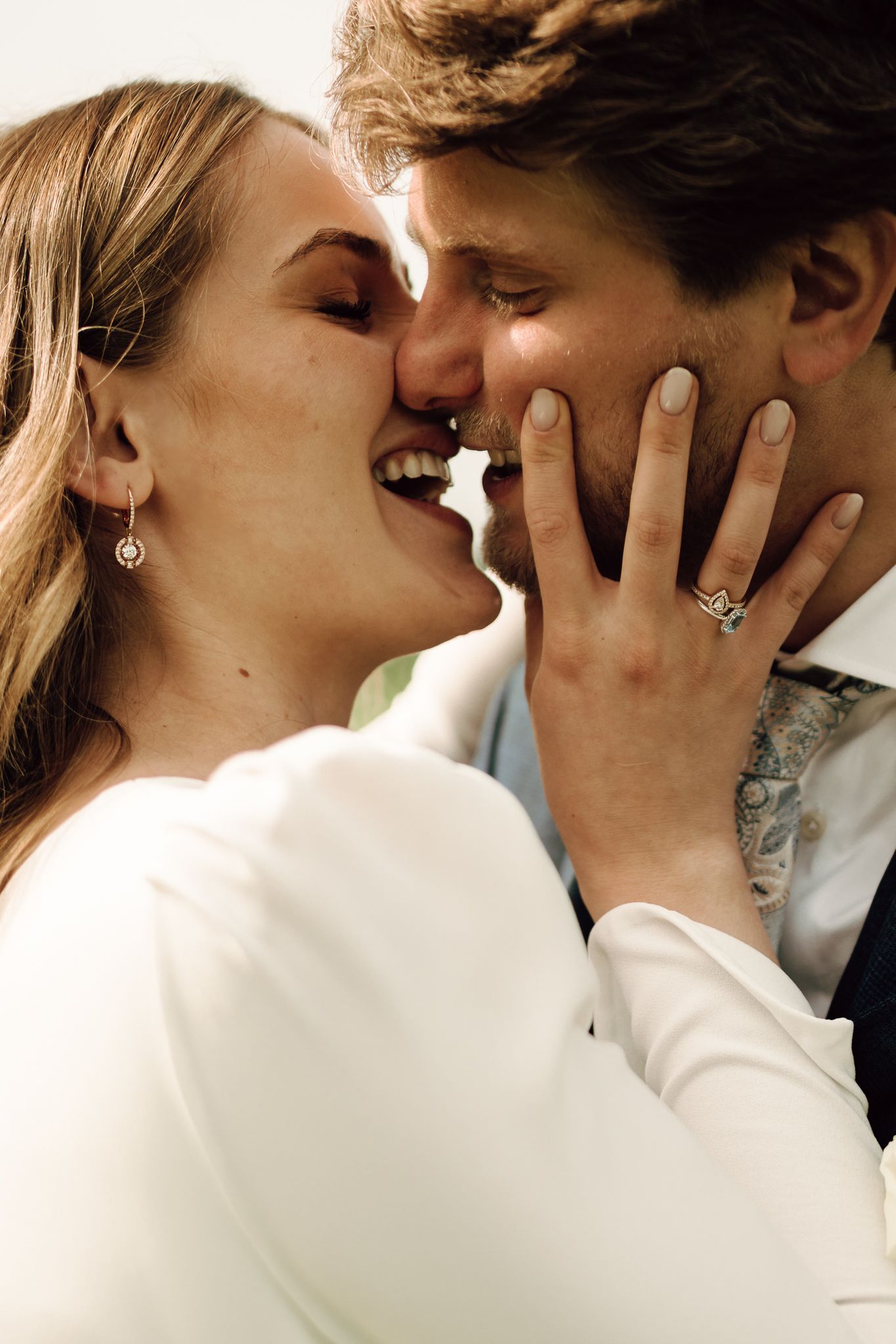 Smiling bride and groom sharing a joyful kiss, showcasing her elegant engagement ring.