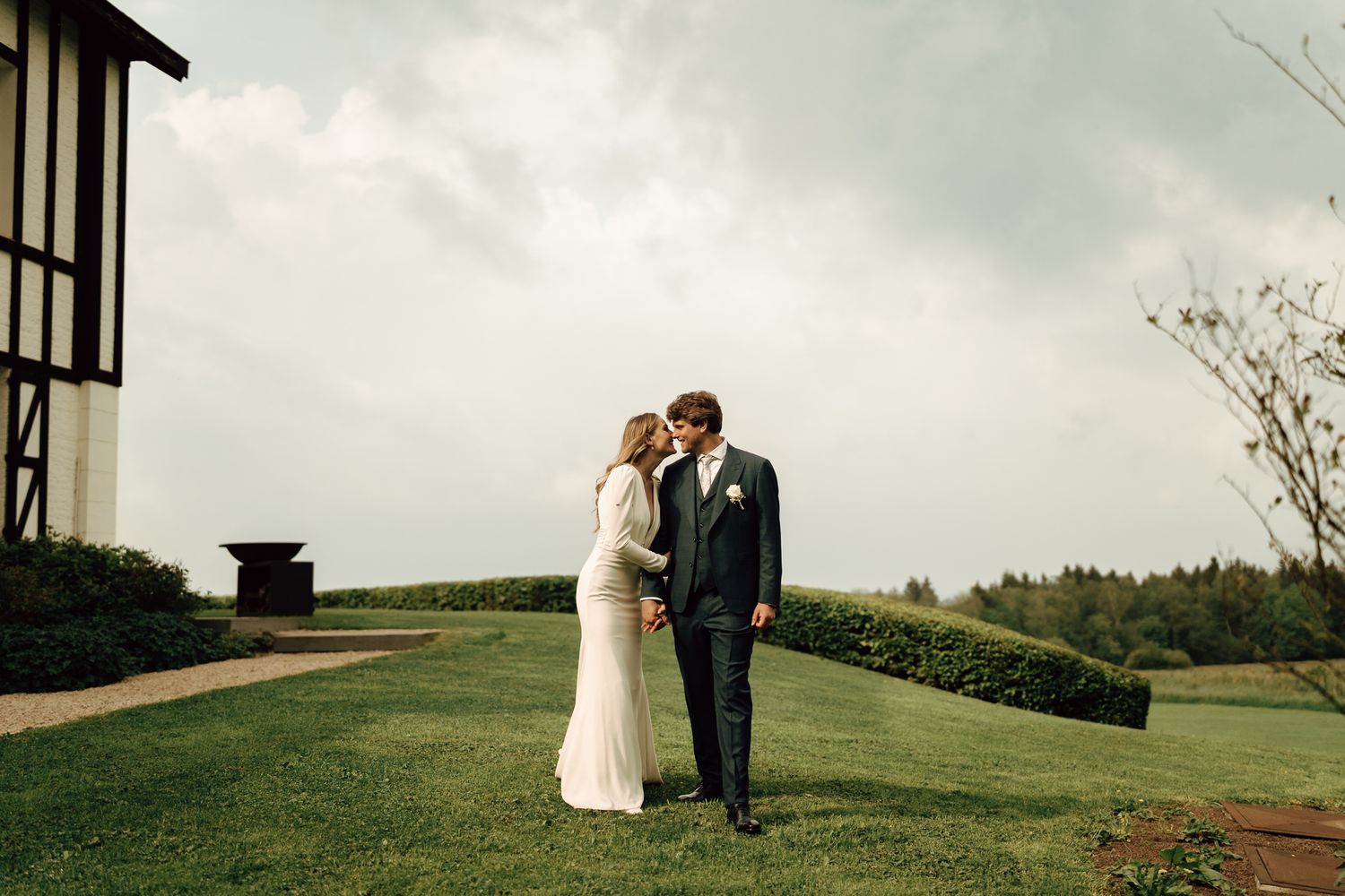 Bride and groom sharing a romantic kiss on lush green grounds of a countryside estate.