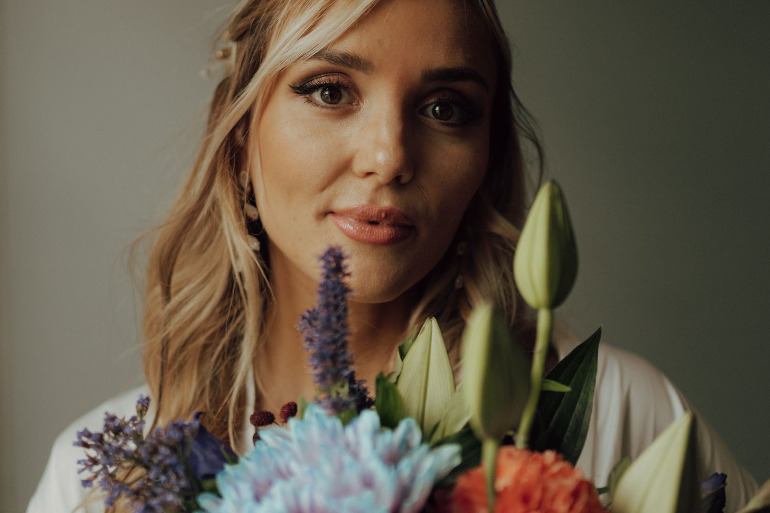 Close-up portrait of smiling bride holding vibrant bouquet with tulips and blue flowers.