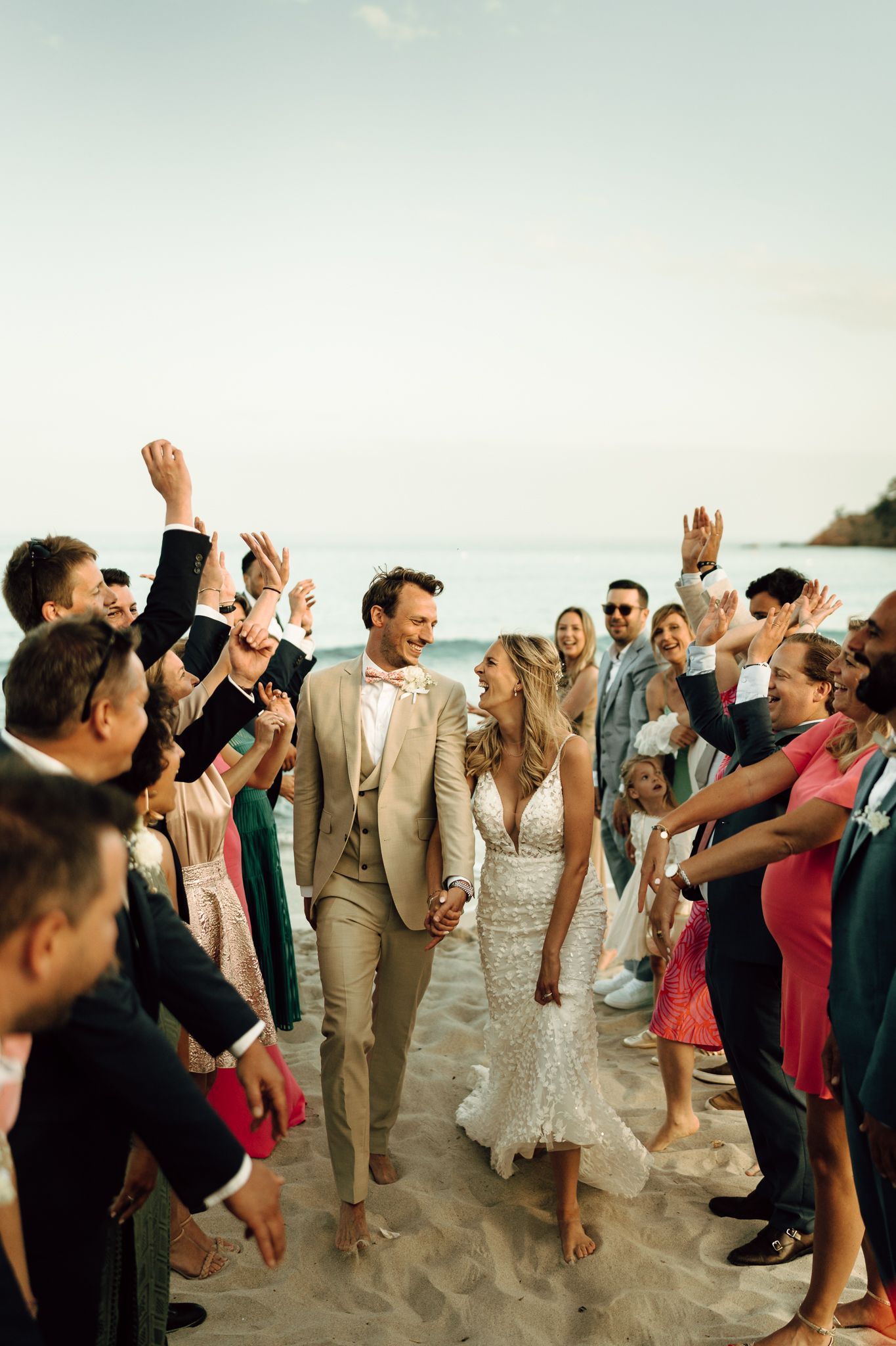 Newlyweds walk through cheering wedding guests lining the sandy beach in a joyful outdoor ceremony exit.
