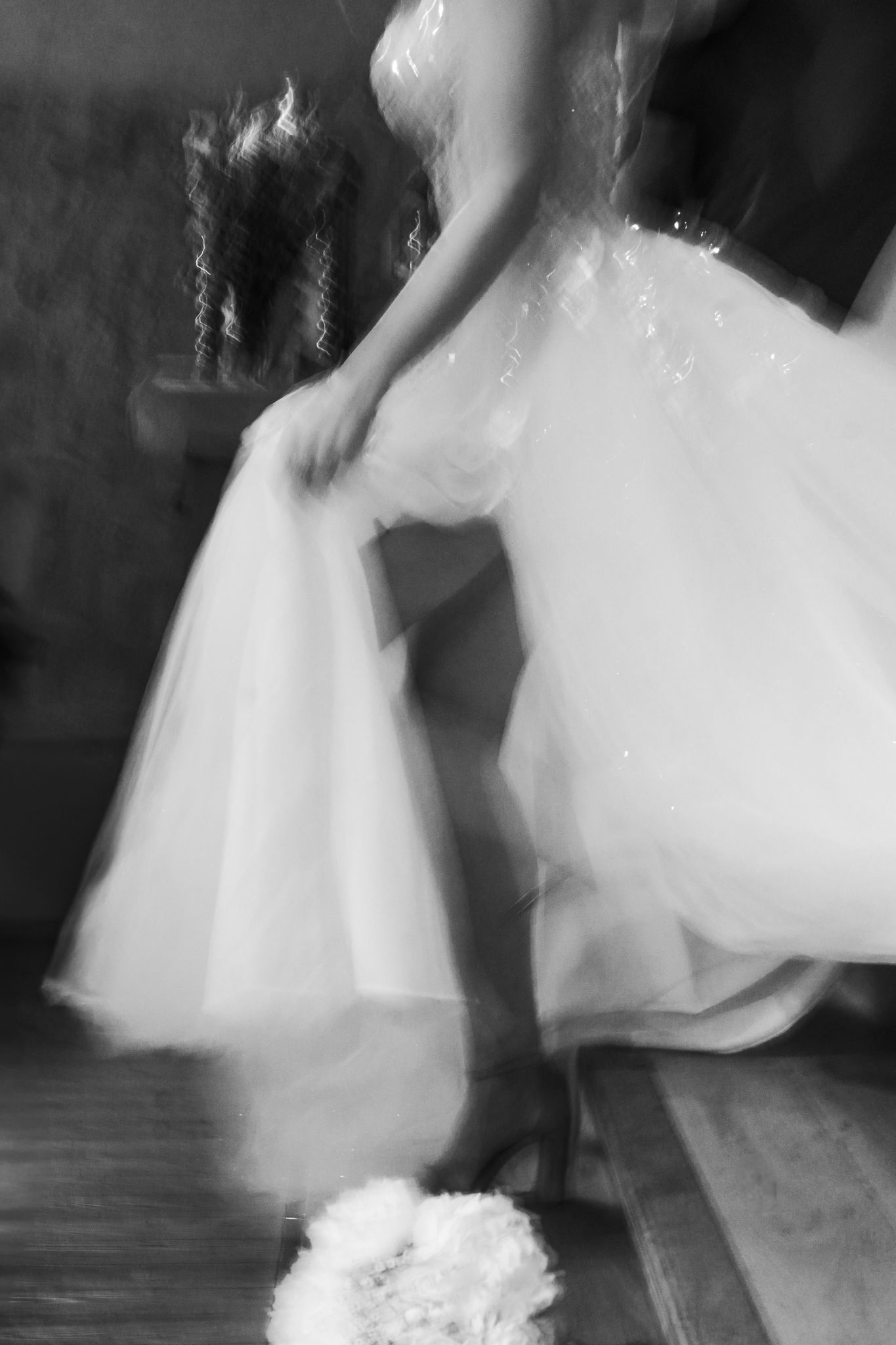 Blurred black and white motion shot of bride in flowing white tulle wedding dress with bouquet.