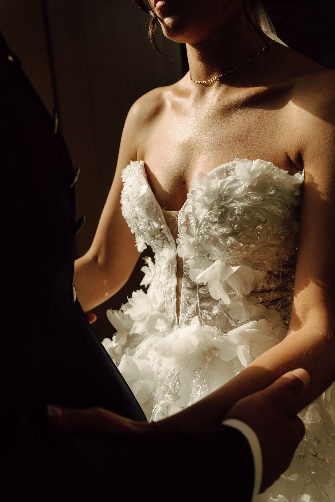 Close-up of bride in strapless ruffled lace wedding gown holding grooms hands in dramatic light.