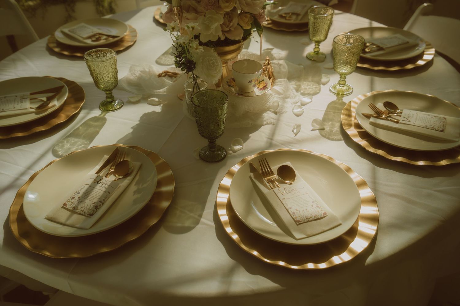Elegant gold and white table setting with charger plates, folded napkins, glassware, and floral centerpiece for a formal event.