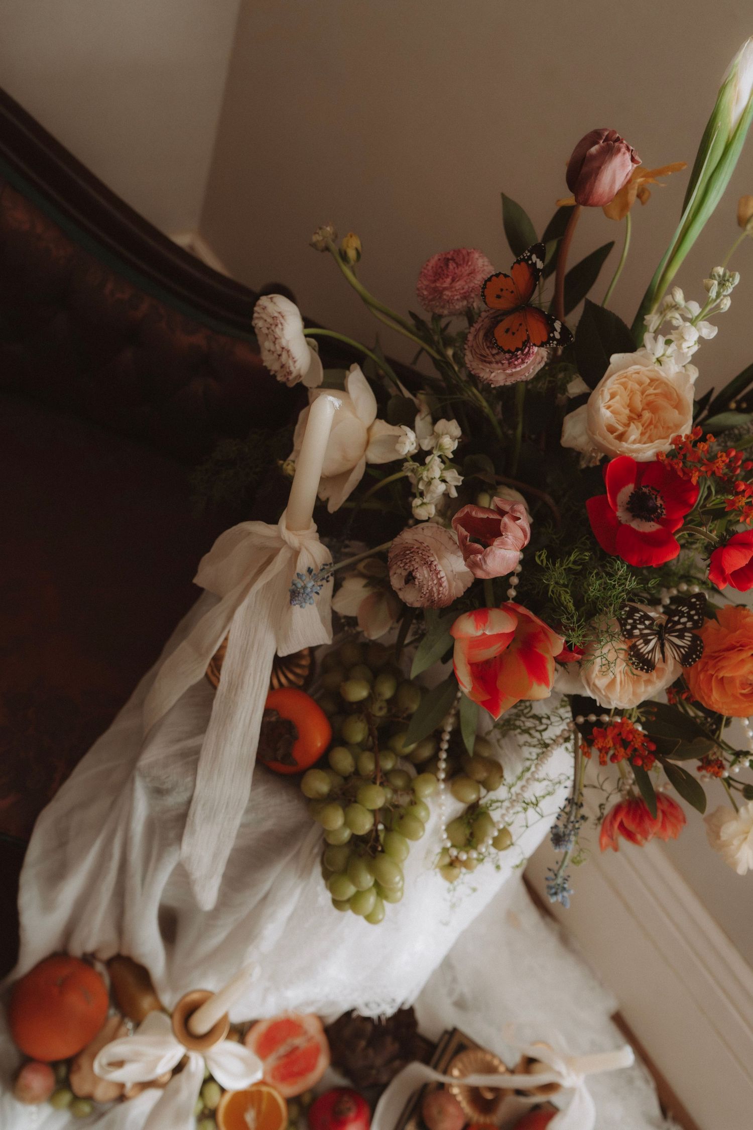 Elegant wedding floral arrangement with red poppies, tulips, and fresh fruit on a draped table.