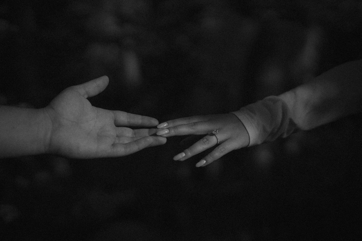 Two hands reaching toward each other in a black and white photo, symbolizing connection and human touch.