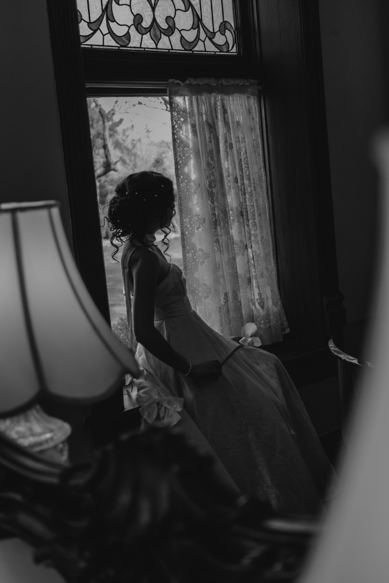 Silhouette of a bride in a white gown standing before an ornate stained glass window.