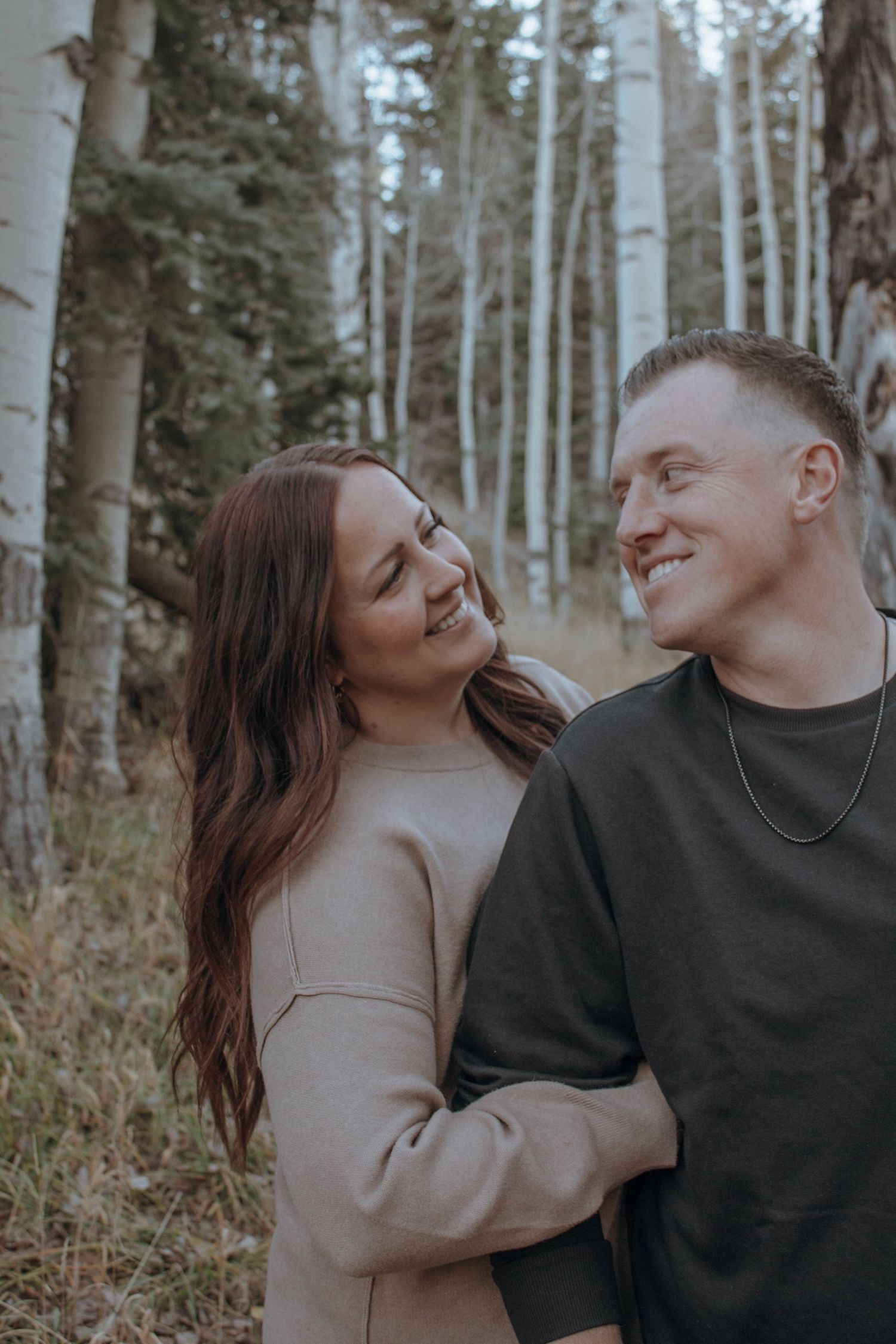 Happy couple embracing and smiling at each other in a birch tree forest during engagement session.