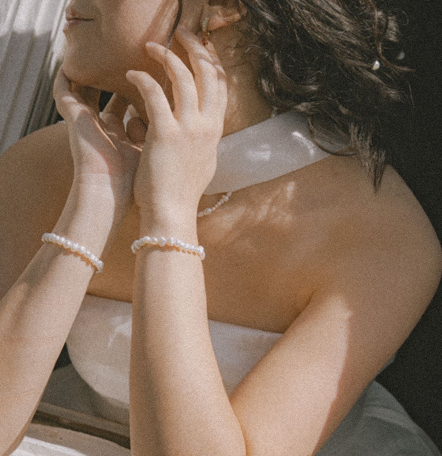 Bride wearing pearl bracelets in a white dress with sunlight casting shadows on her skin.
