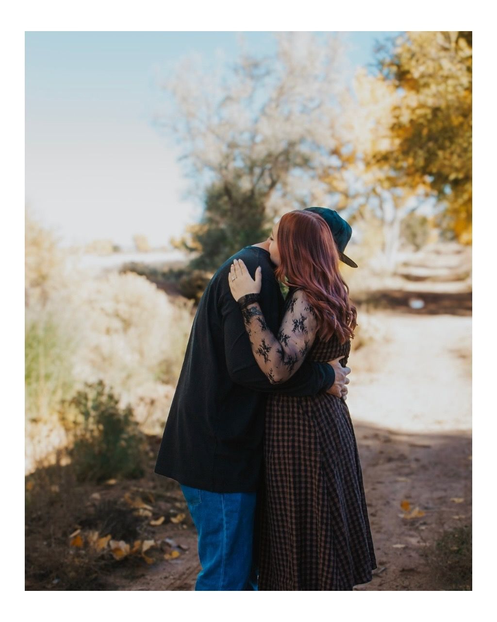 Couple embracing on a nature path surrounded by autumn trees during an outdoor engagement photo session.