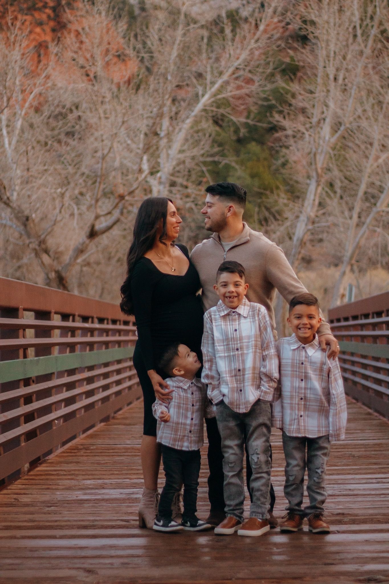 Family of five posing on a wooden bridge surrounded by autumn trees during a warm outdoor photo session.