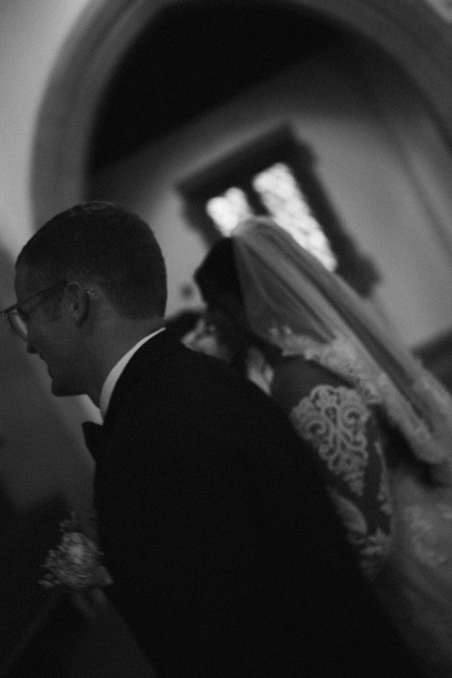 Black and white wedding photo of bride in lace gown and veil walking with groom in suit inside a church.