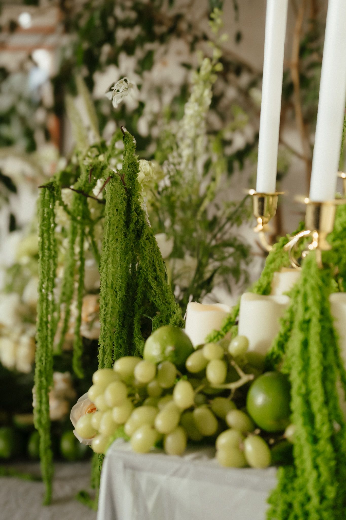 Elegant wedding table decorated with green grapes, cascading amaranthus, white candles, and lush floral arrangements.