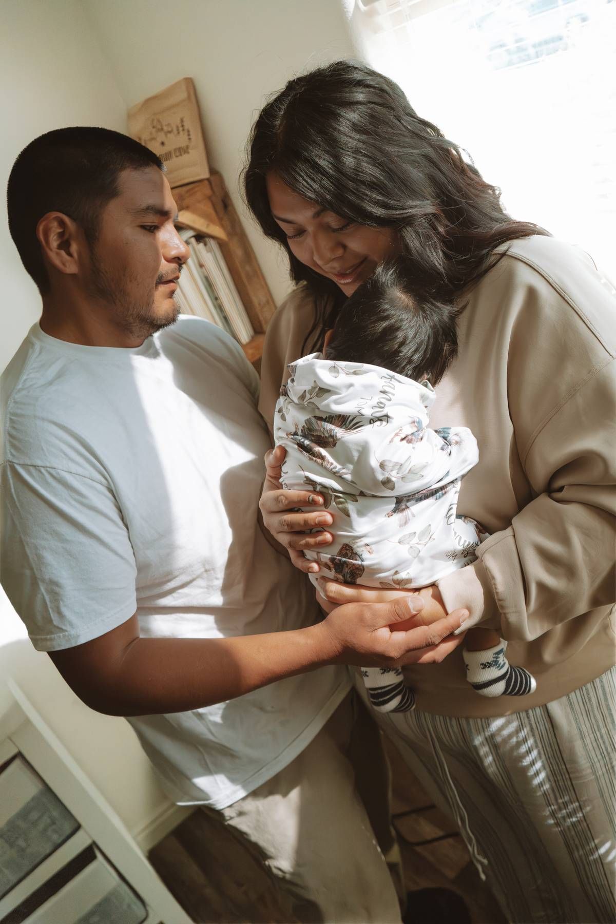 New parents lovingly holding their swaddled newborn baby together in a bright, cozy room.