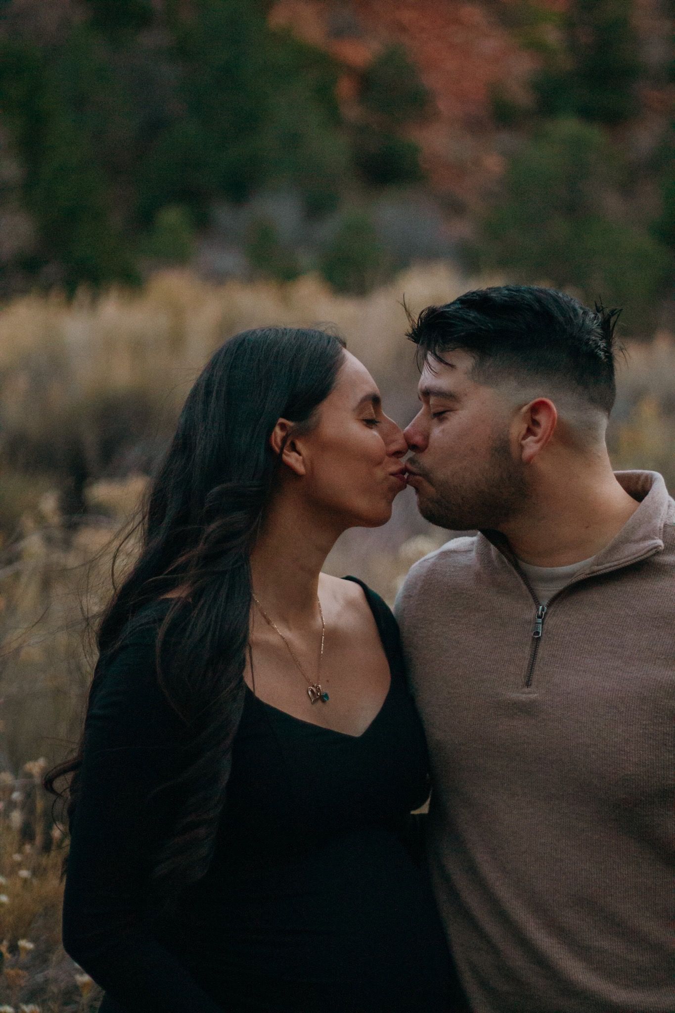 Couple sharing a tender kiss outdoors with colorful fall foliage in the background.
