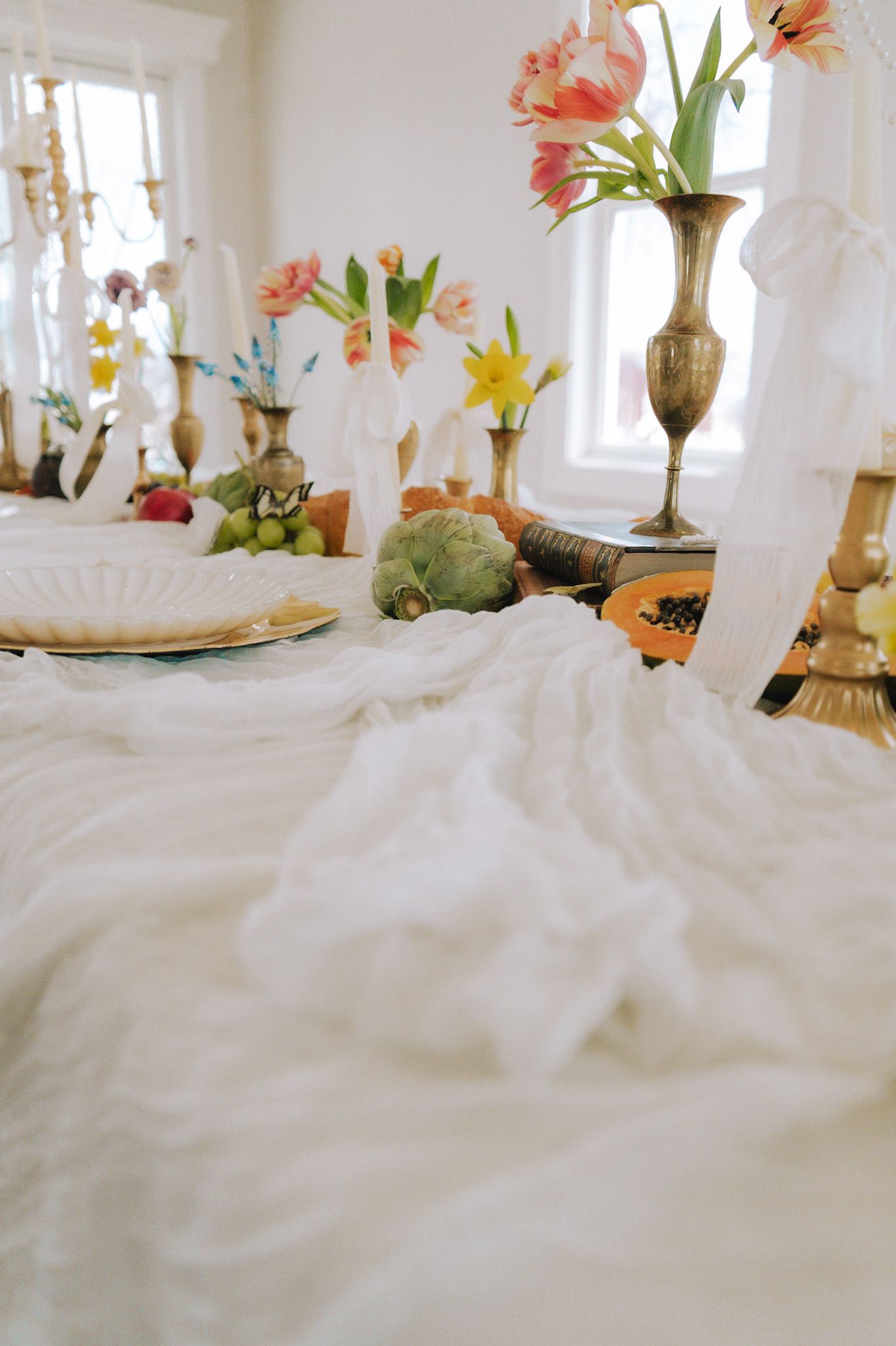 Elegant wedding tablescape with white linen, brass vases, colorful tulips, fruit, and candles.